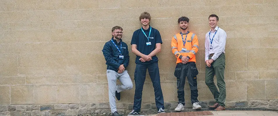 Group of apprentices leaning against a wall outside smiling