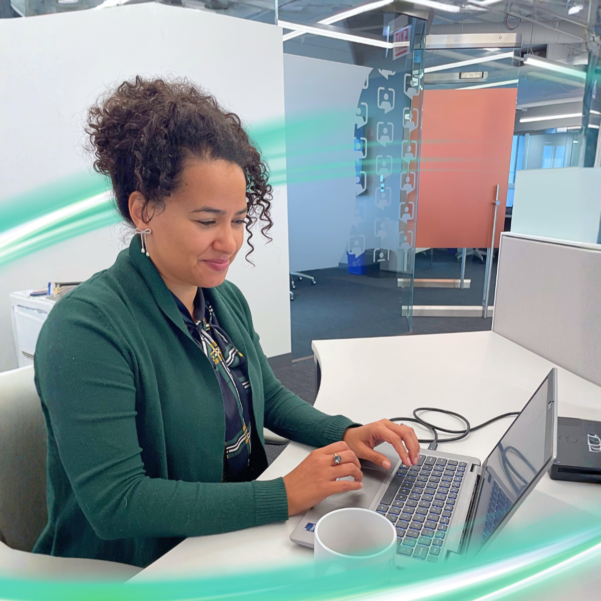 A woman is sitting wearing a green sweater with a slight smile on her face. She has a computer in front of her. There is a electric teal and light green neon oval over the photo.