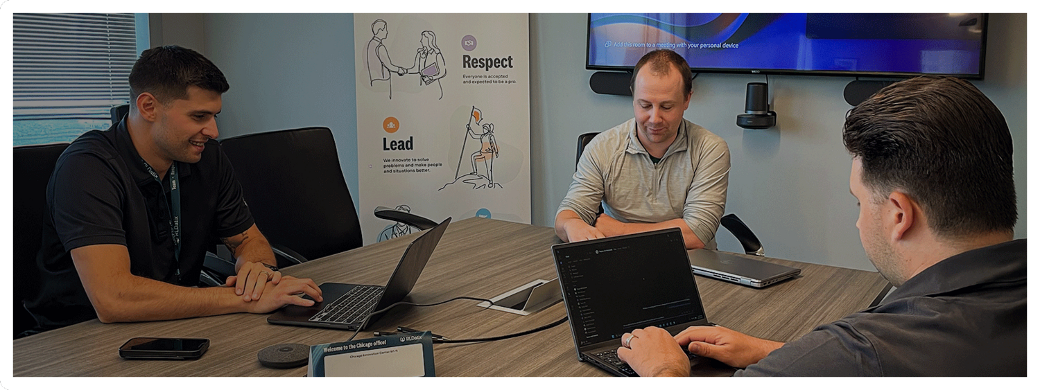 Three employees are together at a table working on computers.