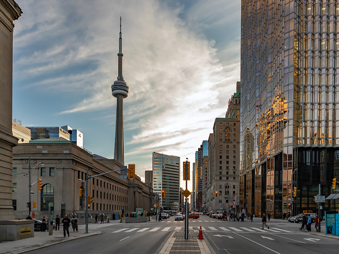 The city streets of Toronto at a streetlight with buildings on either side. It is the evening with a blue and clouded sky. There is a electric teal and light green neon oval over the photo.