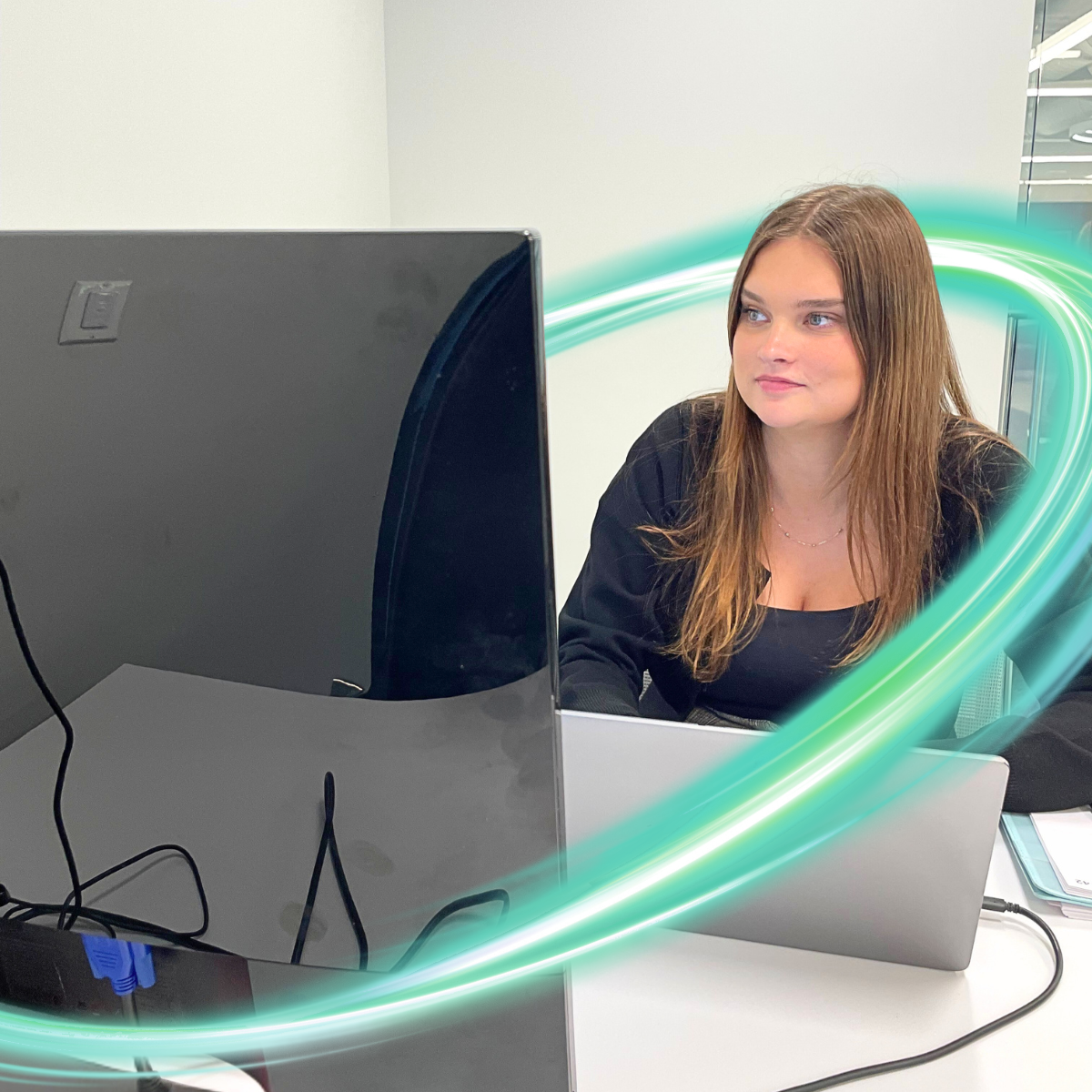 Two women in business clothes are looking at a screen and one is pointing. There is a electric teal and light green neon oval over the photo.