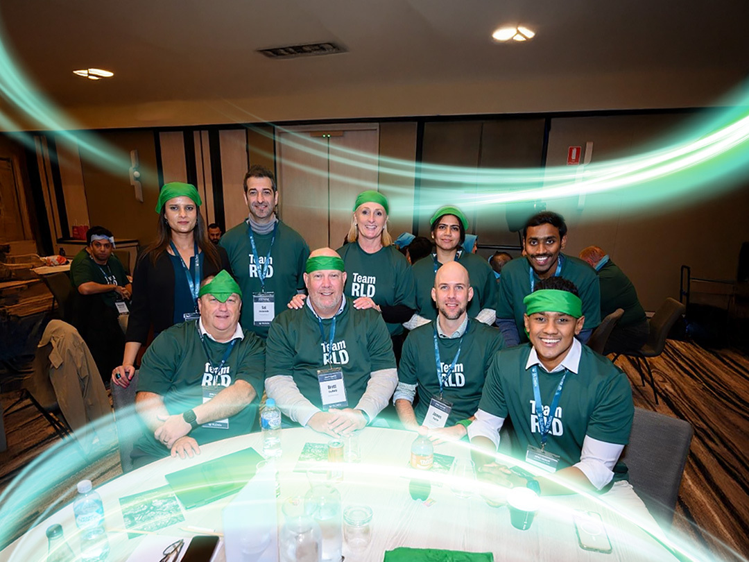 There are nine people looking at the camera in green Team RLD shirts. There is a electric teal and light green neon oval over the photo.