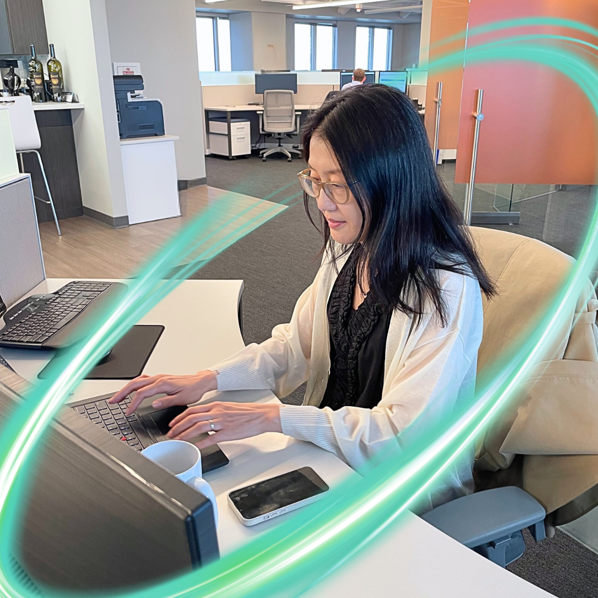 A woman is sitting at a computer with her hands on the keyboard. There is a electric teal and light green neon oval over the photo.