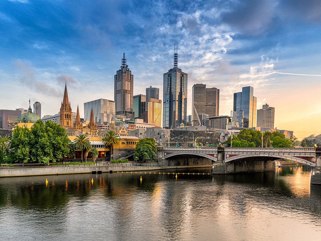 The city skyline of Melbourne and the river in the front. It is the evening with a blue and clouded sky. There is a electric teal and light green neon oval over the photo.