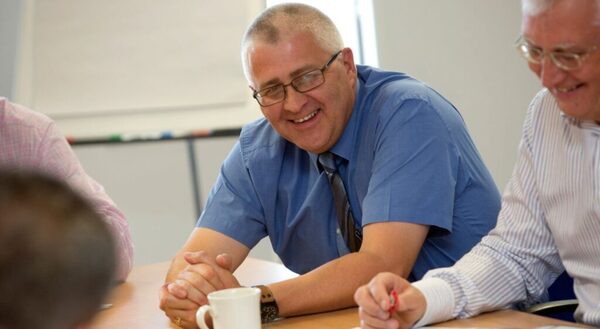 A man smiling while sitting at a desk with a cup of tea